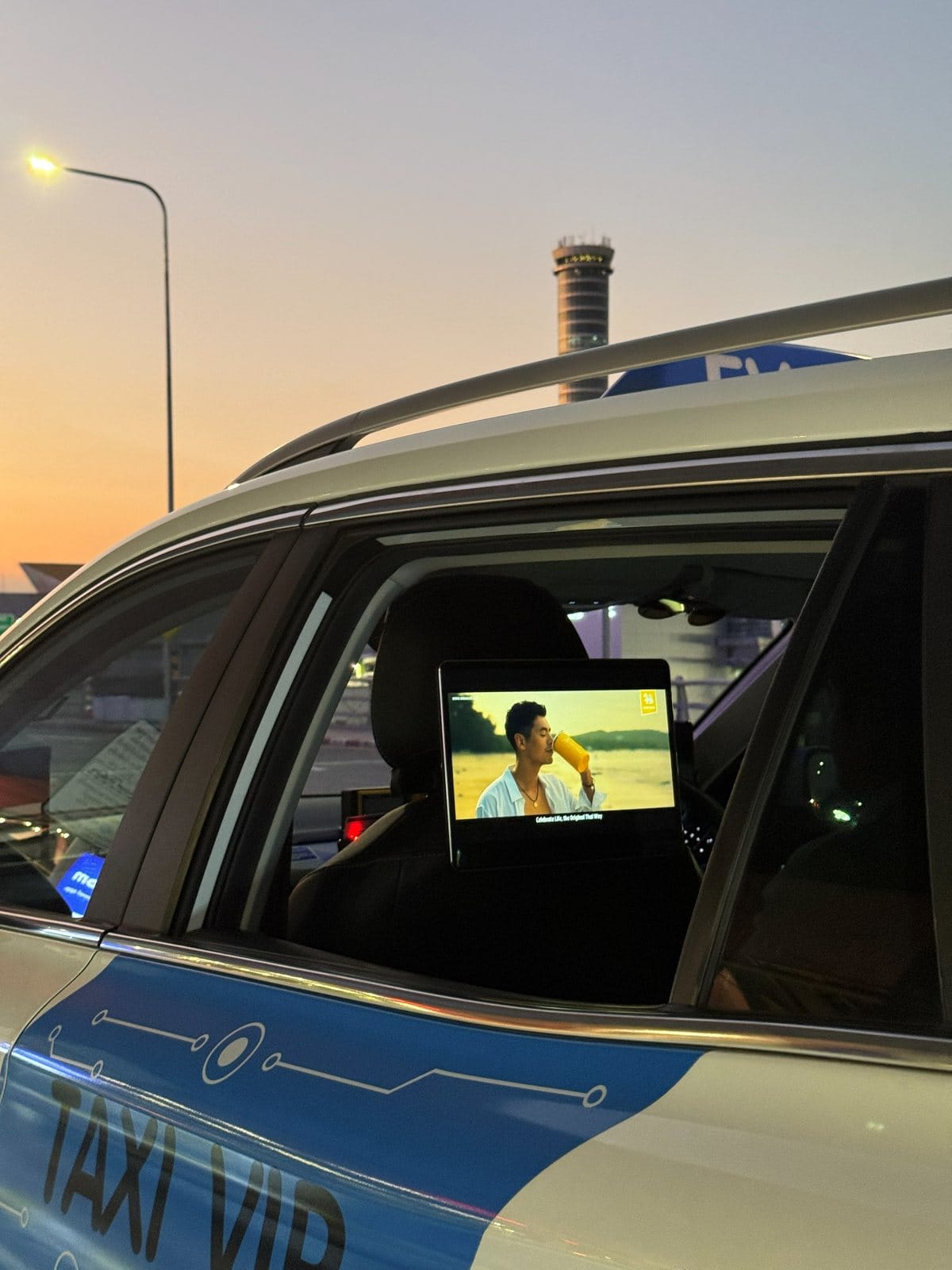 Digital screen on a taxi seat headrest playing an ad while the taxi waits near the airport at dusk