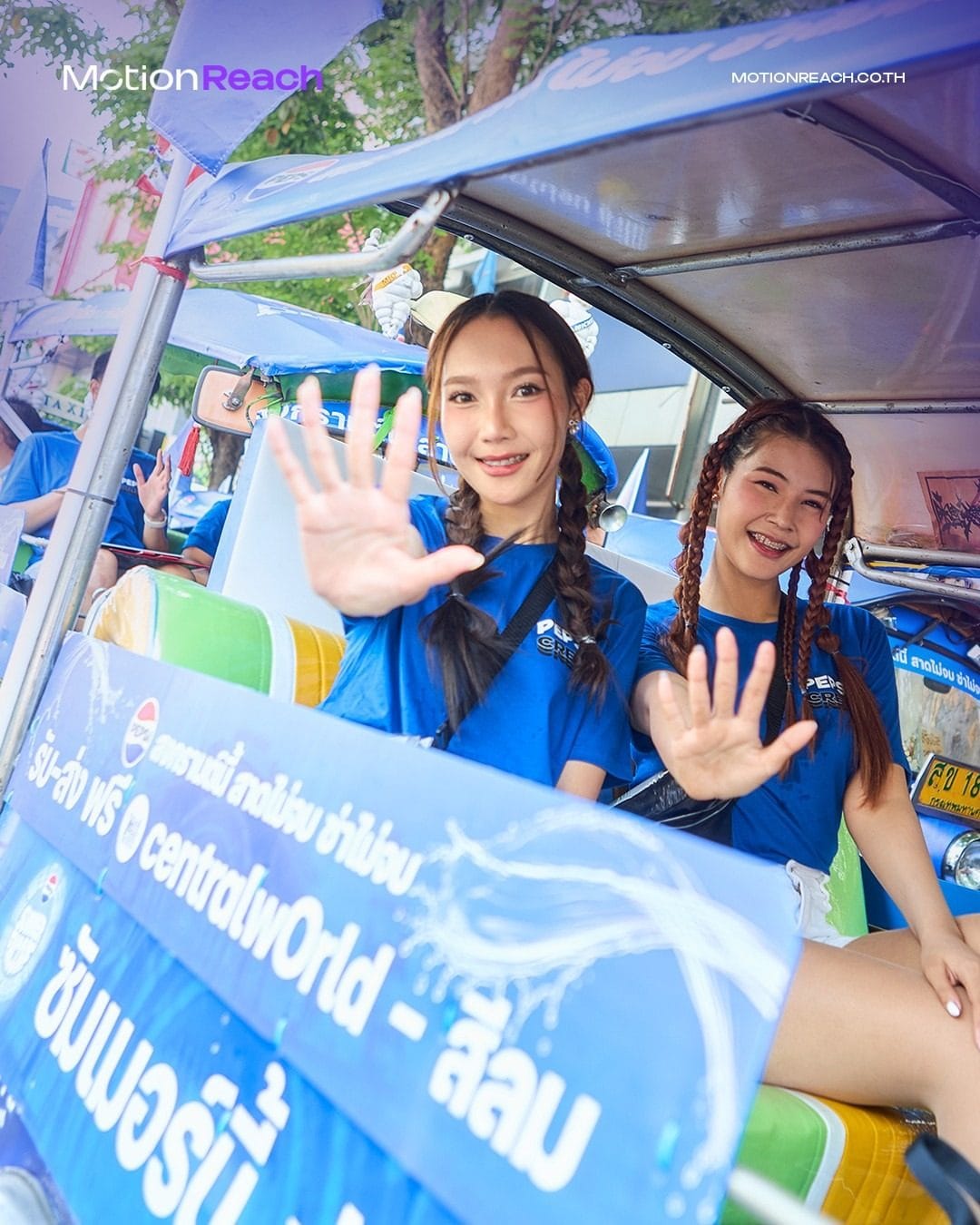 Two women in blue Pepsi shirts waving from a Pepsi-wrapped tuk-tuk